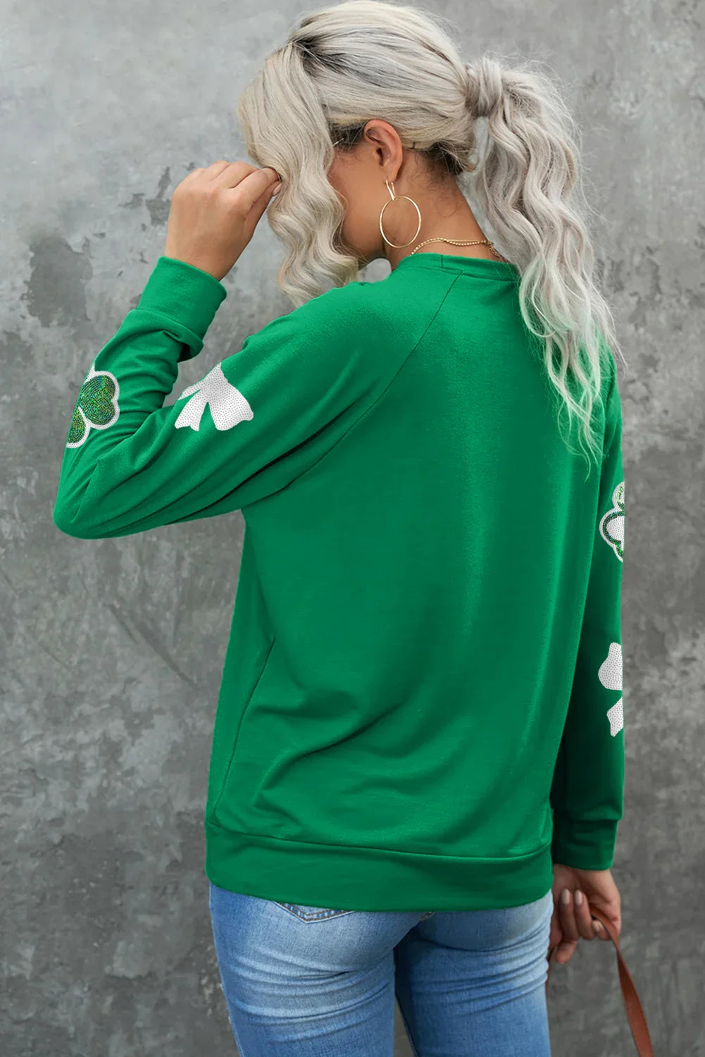 Person wearing a green sweatshirt with white designs on a gray background