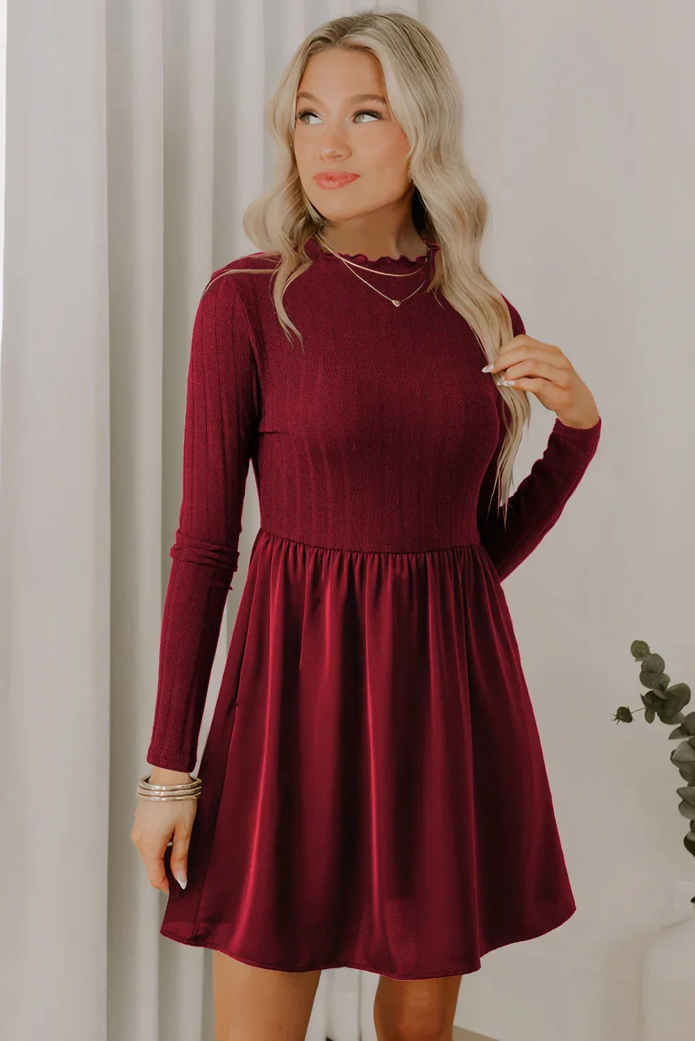 Blonde woman wearing a burgundy long-sleeve dress with ribbed knit bodice and flowy skirt, indoors