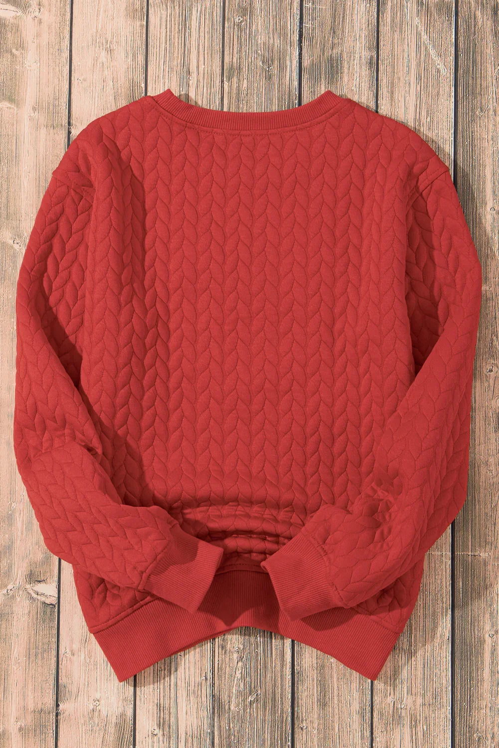 Red quilted sweater with textured cable knit pattern on rustic wooden floor