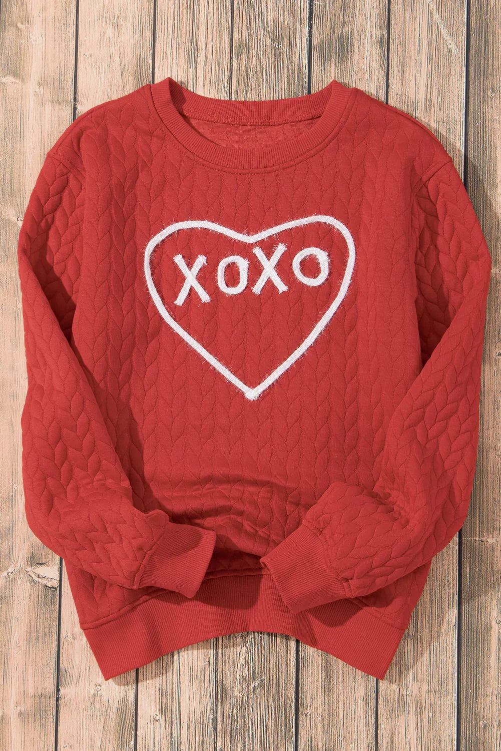 Red quilted sweatshirt with white heart and XOXO design on wooden floor background