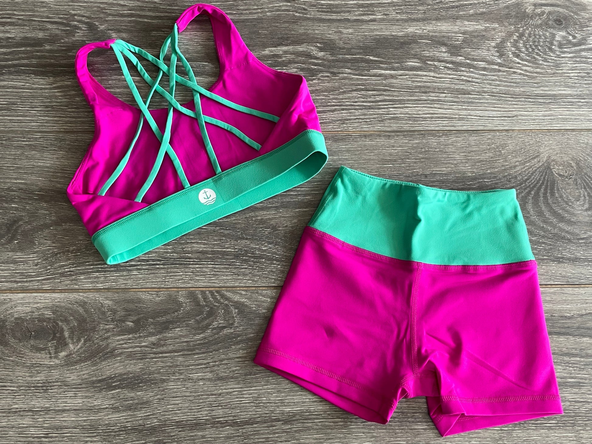 lie flat mockup of a horizon girls dancewear hot pink top with teal cross straps and bottoms in hot pink and teal accents.