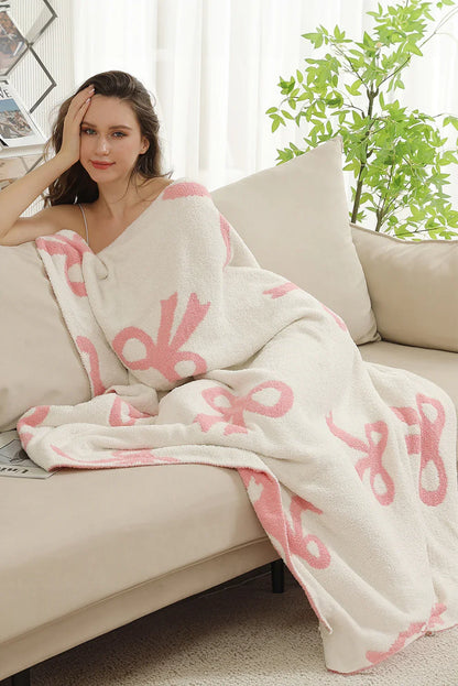 Young woman wrapped in cozy white blanket with pink bow patterns lounging on beige sofa