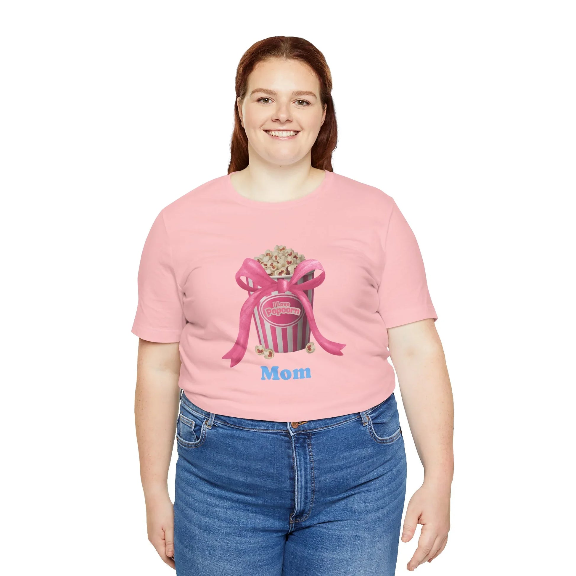 Smiling woman wearing pink T-shirt with popcorn bucket graphic and Mom text paired with blue jeans
