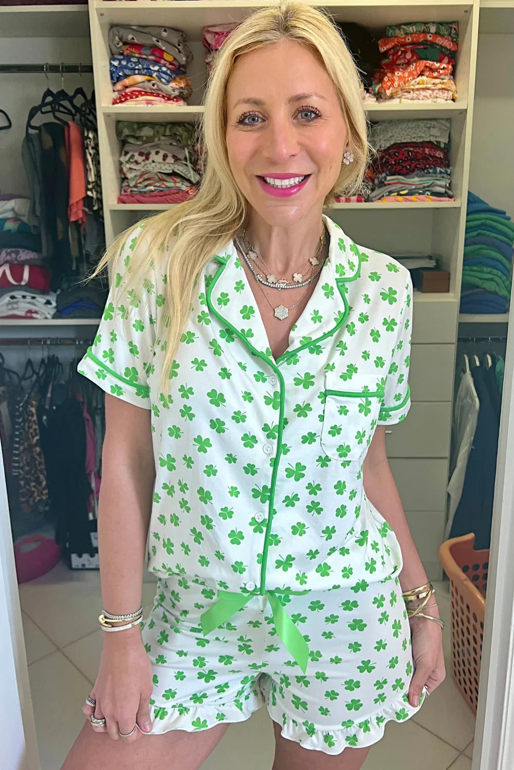 Woman wearing a green and white shamrock patterned pajama set in a room with shelves of folded clothes.