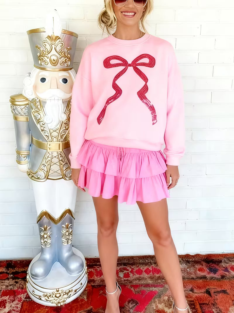 Woman in pink outfit with large red bow standing next to a nutcracker figurine.