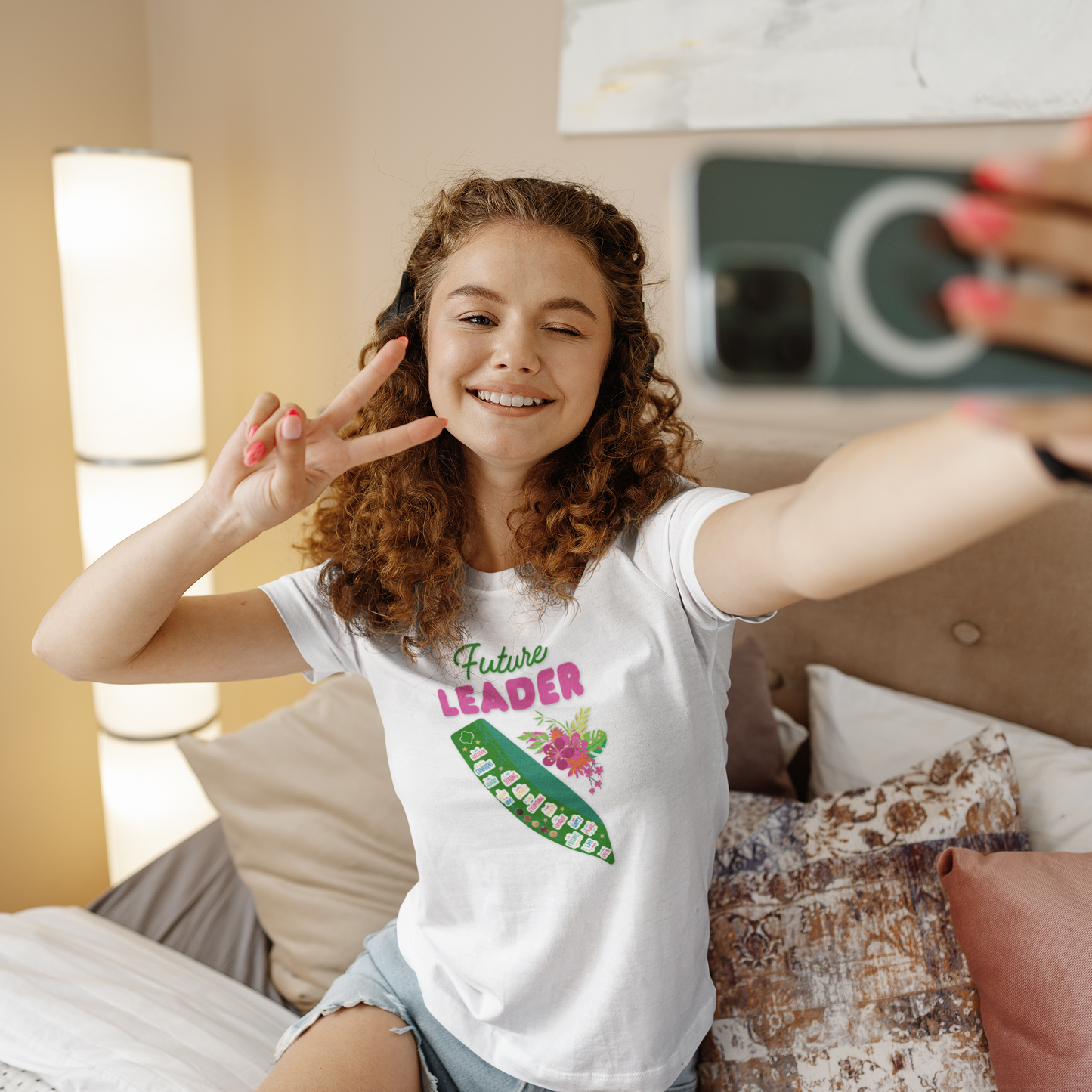 Young girl taking a selfie in a bedroom wearing a 'Future Leader' t-shirt.