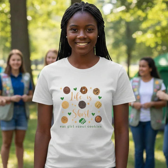 Girl wearing a t-shirt with a cookie-themed design, standing in a park with other girls in the background.