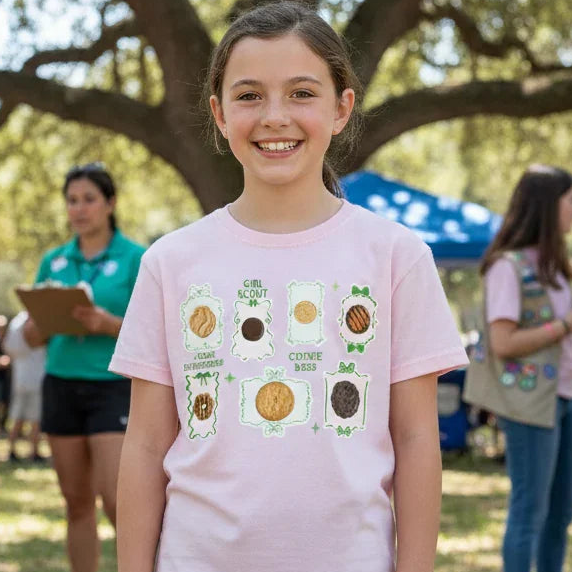 Girl in a pink t-shirt with a science-themed design standing outdoors with people and trees in the background.