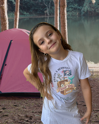 Young girl standing in front of a pink tent by a lake with trees in the background wearing a girl scout camporee tee