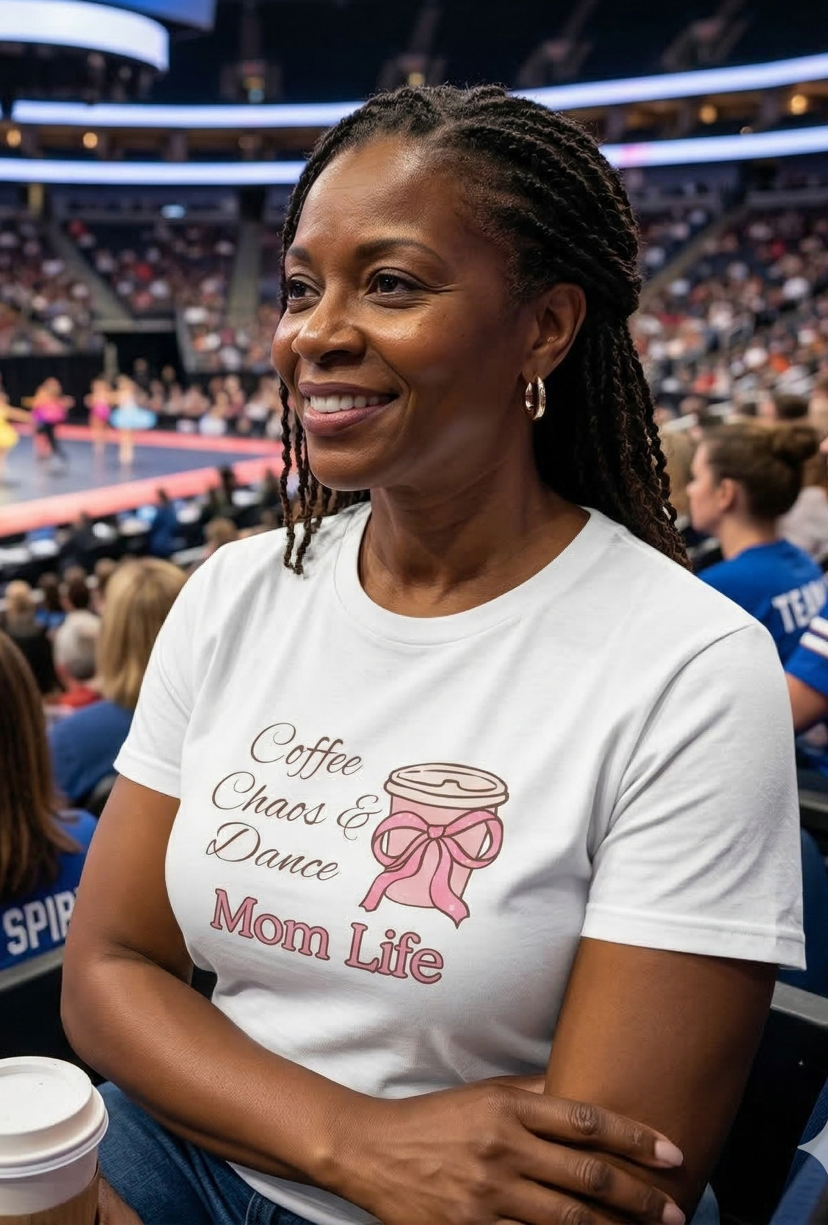 Woman wearing a 'Coffee, Chaos & Dance Mom Life' t-shirt in a sports arena.