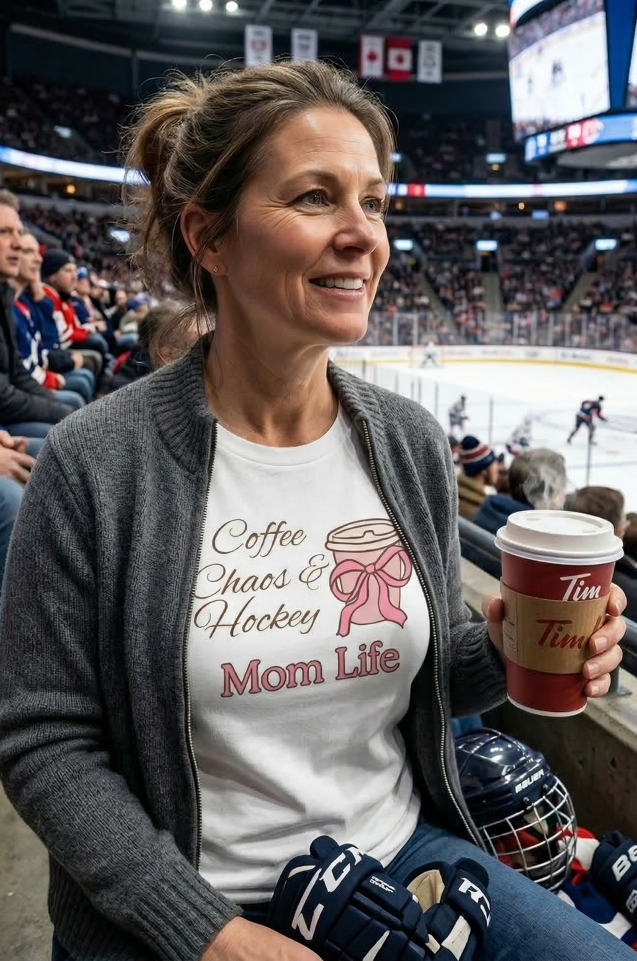 Woman at a hockey game wearing a 'Coffee, Chaos & Hockey Mom Life' shirt and holding a Tim Hortons cup.
