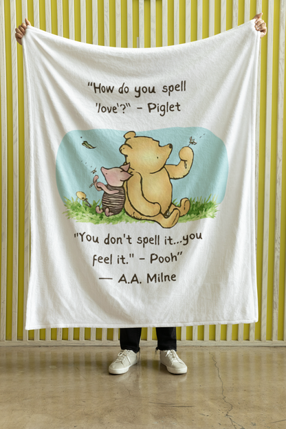 Person holding a Winnie the Pooh and Piglet 50" x 60" blanket with a quote against a striped wall.