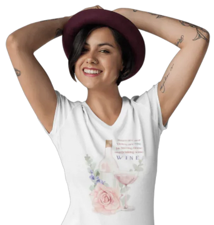 Woman wearing a white t-shirt with floral design and text "Roses Are Red, Violets are FINE, I'm Staying Home and Drinking WINE", posing with hands behind her head on a white background.