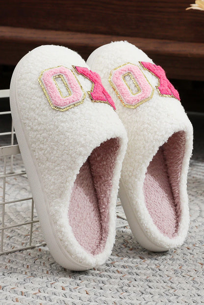 White fuzzy slip-on slippers with pink plush interior and embroidered pink and gold XO design