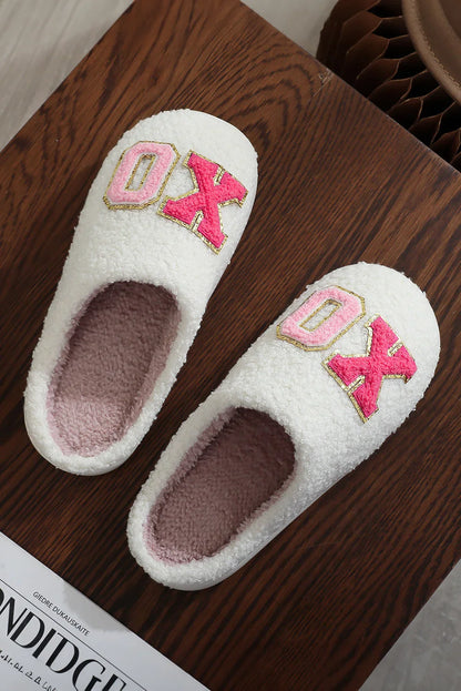 White fuzzy slippers with pink inner lining and pink 'OX' letters on wooden surface