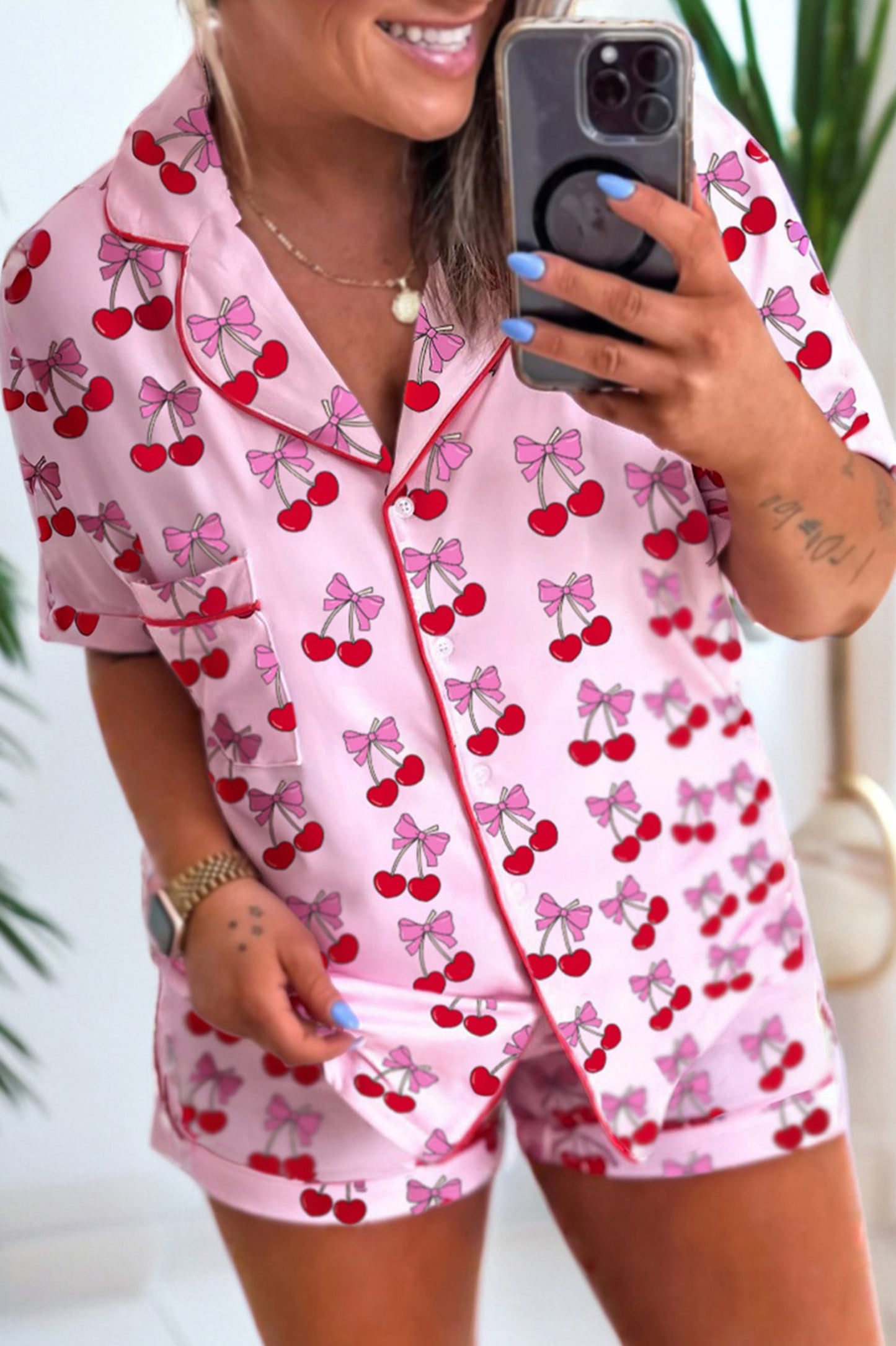 Person wearing pink pajama set with cherry and bow pattern, taking a mirror selfie.