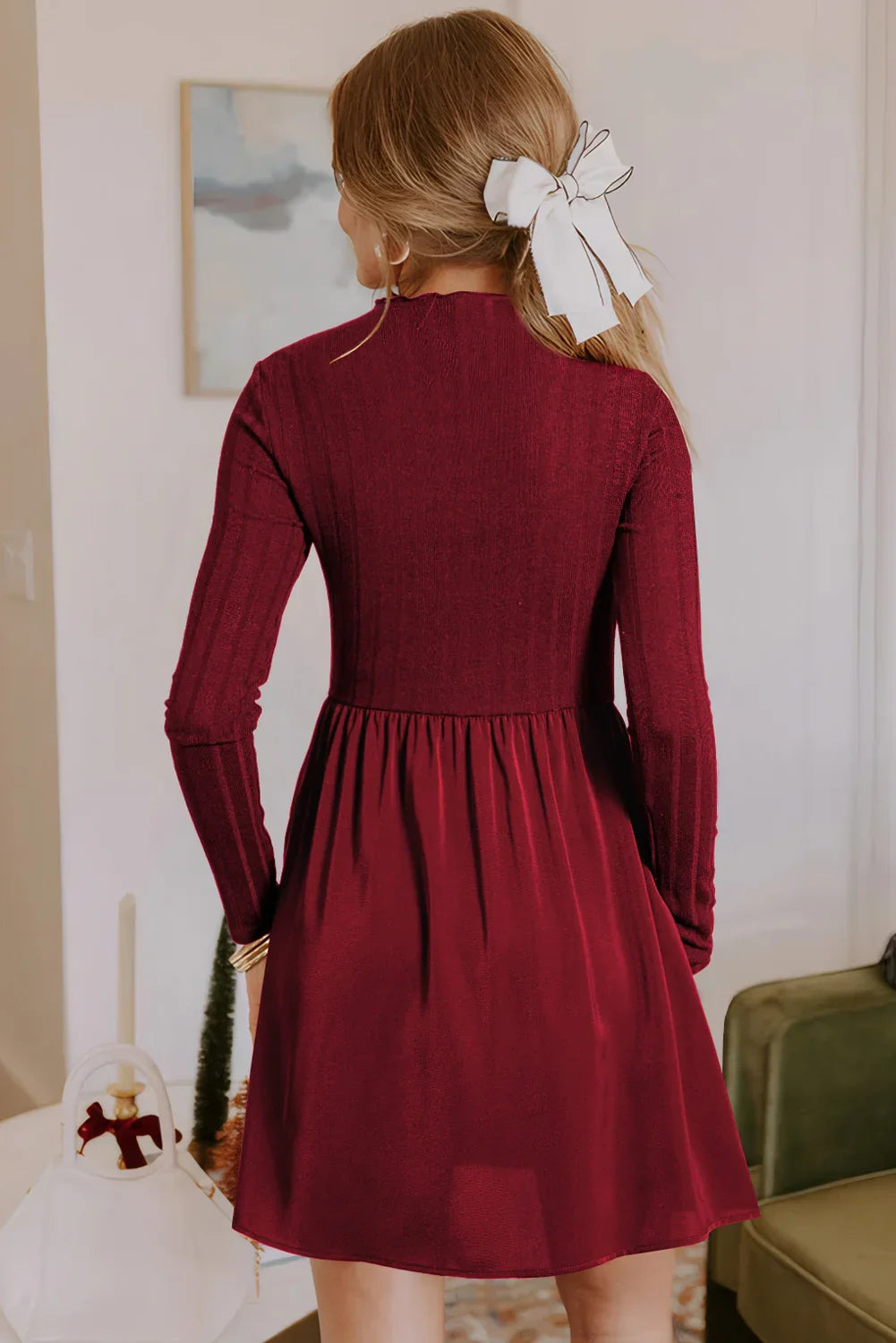 Woman wearing a burgundy ribbed long-sleeve dress with a white hair bow indoors
