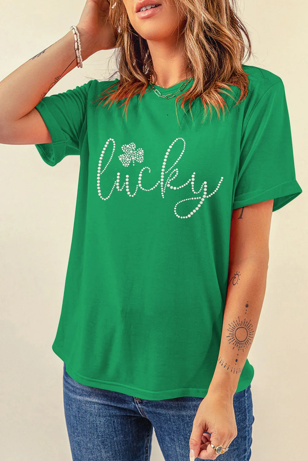 Woman wearing green t-shirt with rhinestone text "lucky" and clover design, casual jeans, and tattoos