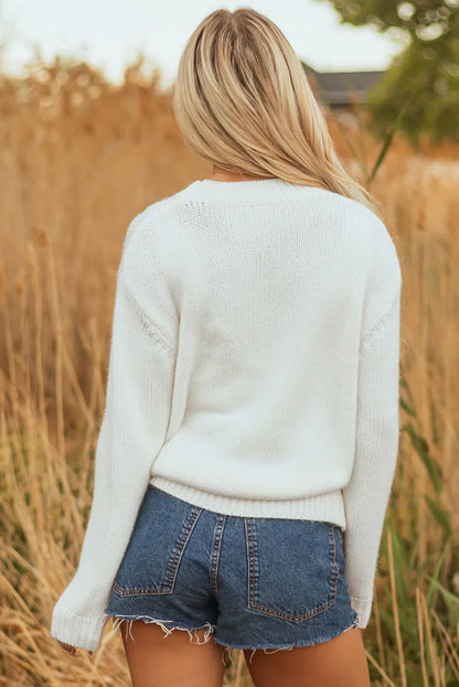 Woman with blonde hair wearing a white knit sweater and denim shorts in a natural outdoor setting