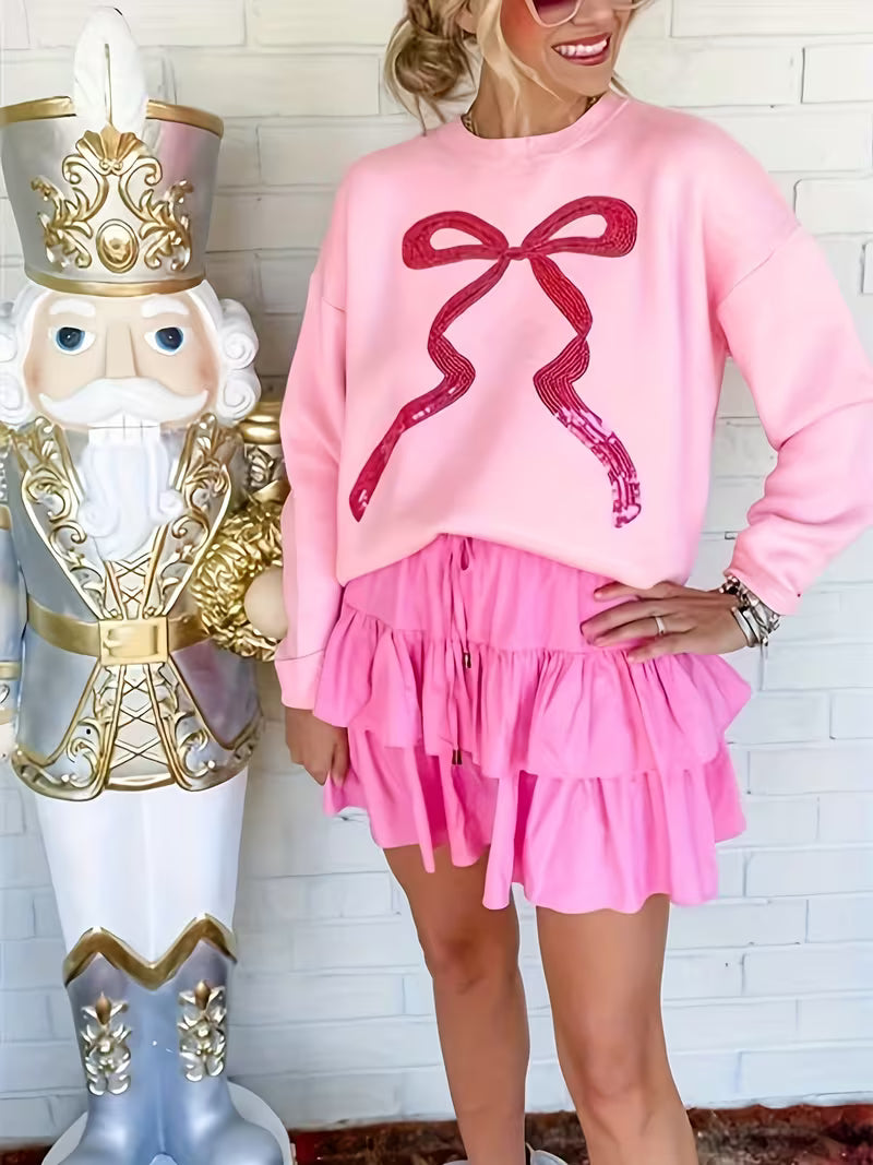 Person wearing a pink sweatshirt with a large red bow design and pink skirt, standing next to a decorative nutcracker.