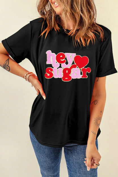 Woman wearing black T-shirt with red and pink glittery text 'hey sugar' and heart design, paired with blue jeans