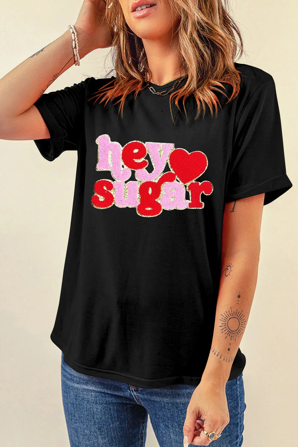 Woman wearing black t-shirt with pink and red 'hey sugar' text and heart graphic, paired with jeans