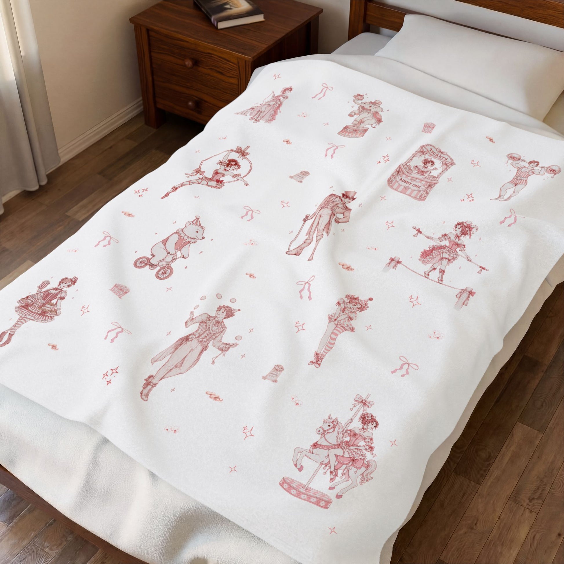 White throw blanket with red and pink coquette circus prints on a wooden floor bedroom setting