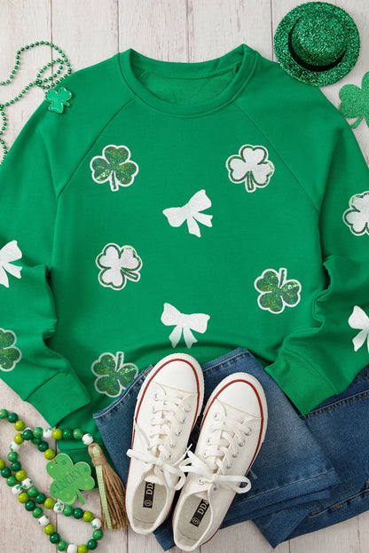 Green sweatshirt with shamrock and bow patterns, paired with white sneakers and St. Patrick's Day accessories on a wooden surface.