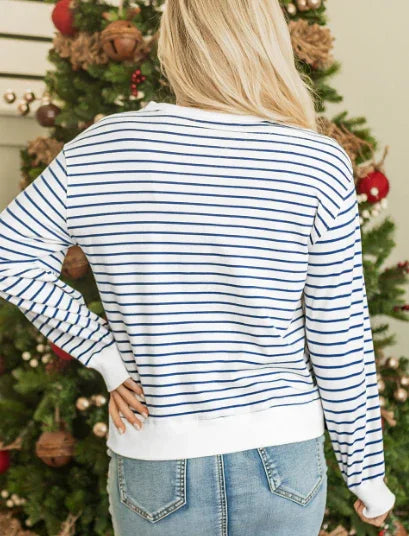 Woman wearing blue and white striped sweater and jeans standing in front of decorated Christmas tree