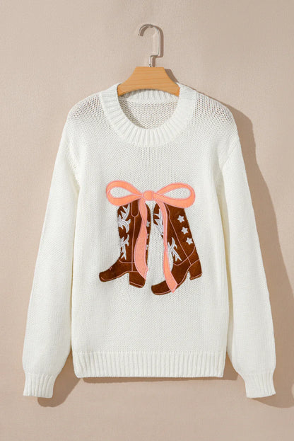 White knitted sweater with embroidered brown cowboy boots and pink bow hanging on wooden hanger