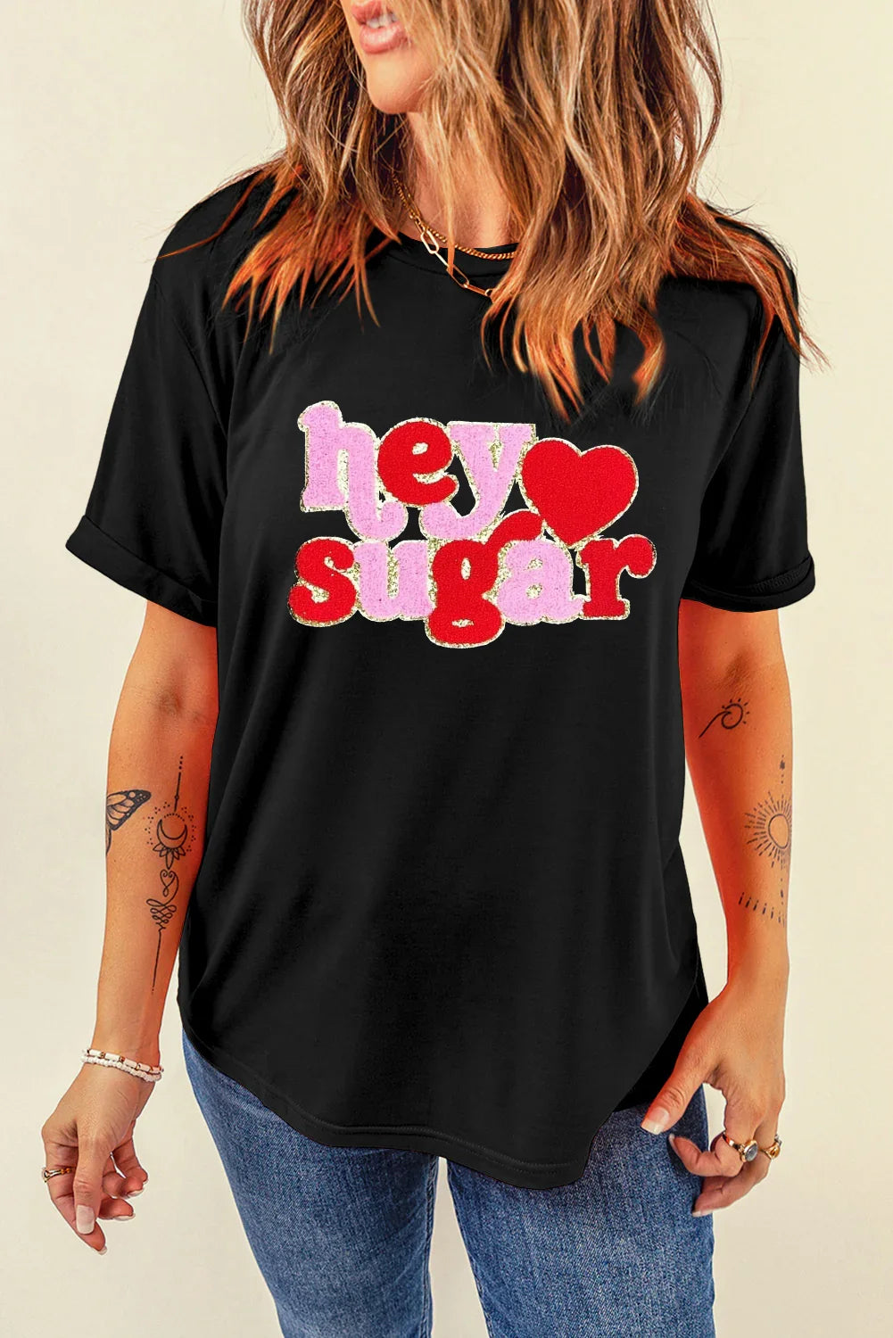 Woman wearing black t-shirt with pink and red text 'hey sugar' and heart graphic, paired with blue jeans