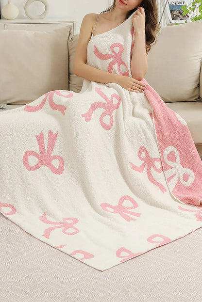 Woman wrapped in soft white and pink throw blanket with bow patterns sitting on beige sofa in cozy living room