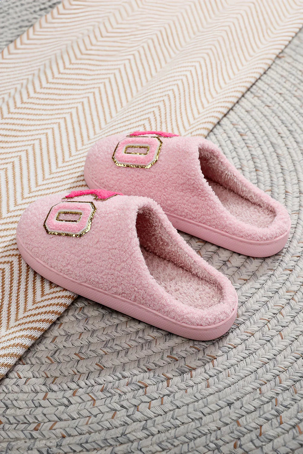 Pair of pink fluffy slippers with gold and pink patch detail on woven round rug and chevron patterned fabric
