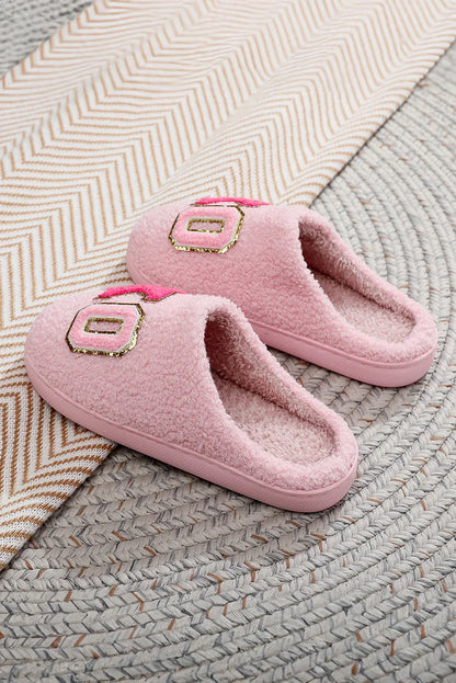 Pair of pink fluffy slippers with gold and pink patch detail on woven round rug and chevron patterned fabric