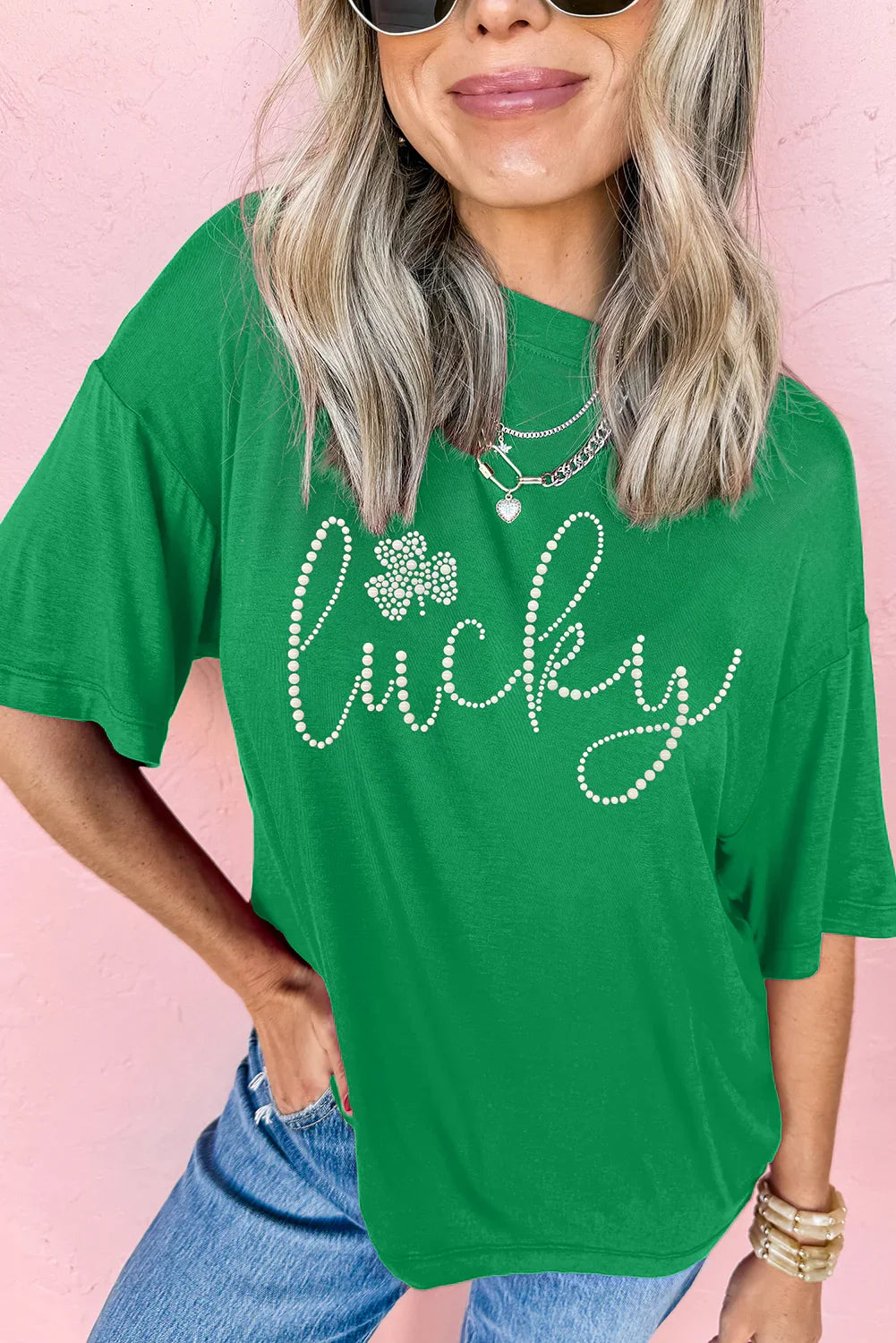 Woman wearing green Lucky t-shirt with rhinestone lettering and shamrock, blue jeans, and layered necklaces