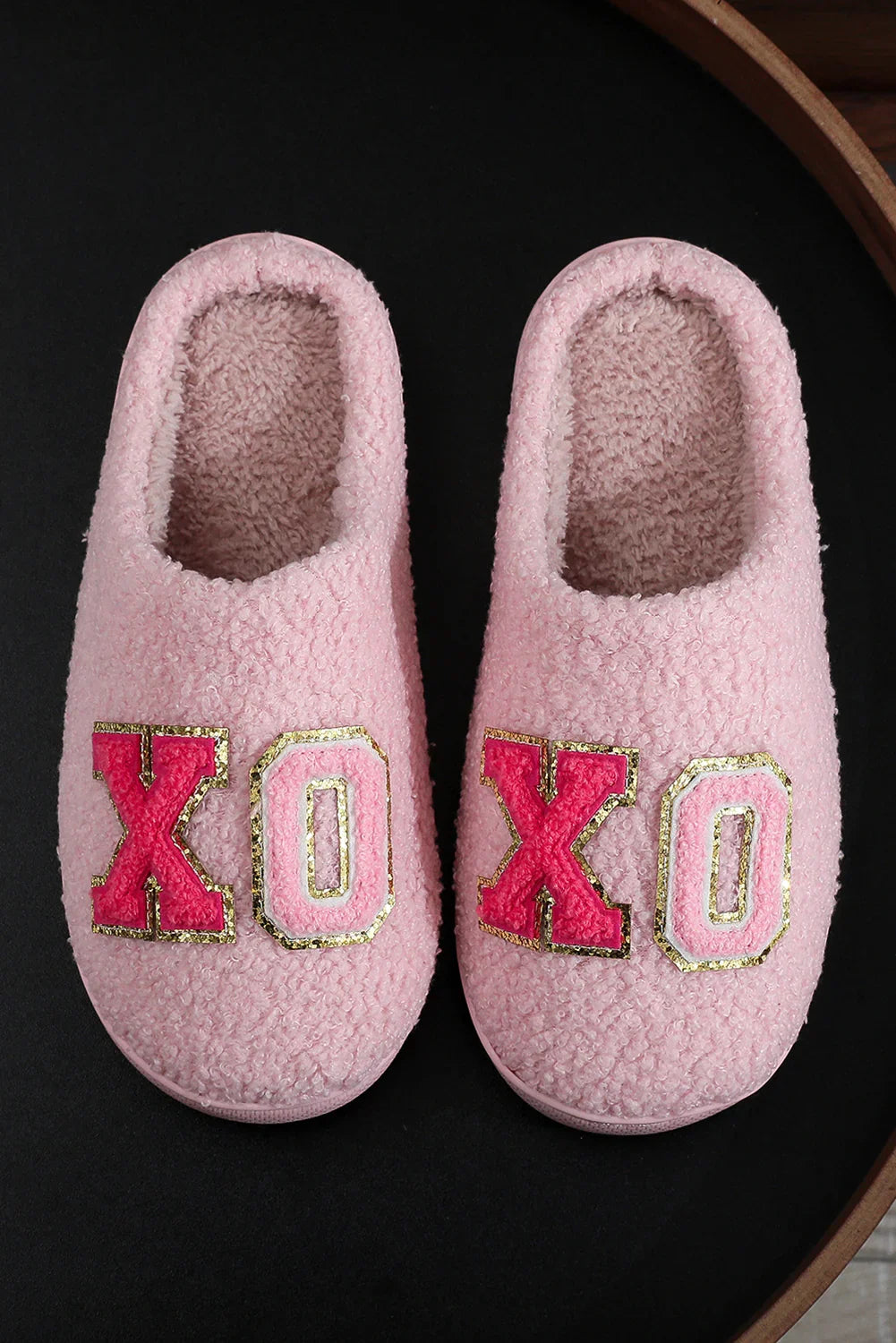 Pink fuzzy slippers with red and pink XO letters outlined in gold on black surface