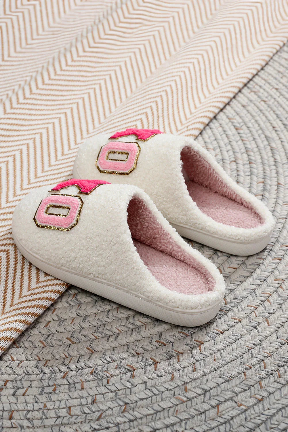 Pair of cozy white fleece slippers with pink letter patches on textured rugs