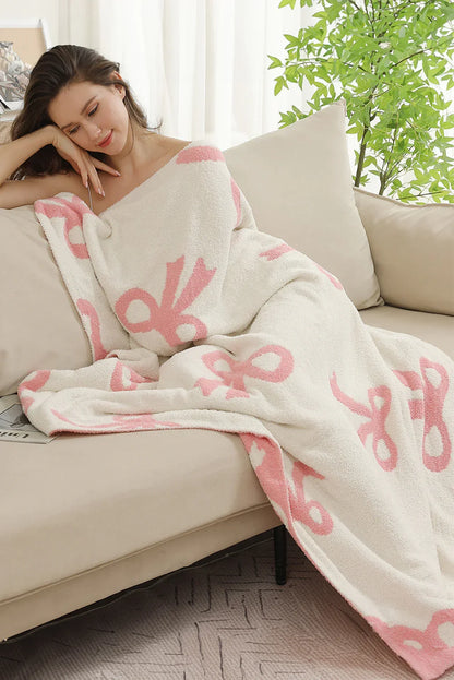 Woman relaxing on beige sofa wrapped in soft white and pink patterned blanket with indoor plant background