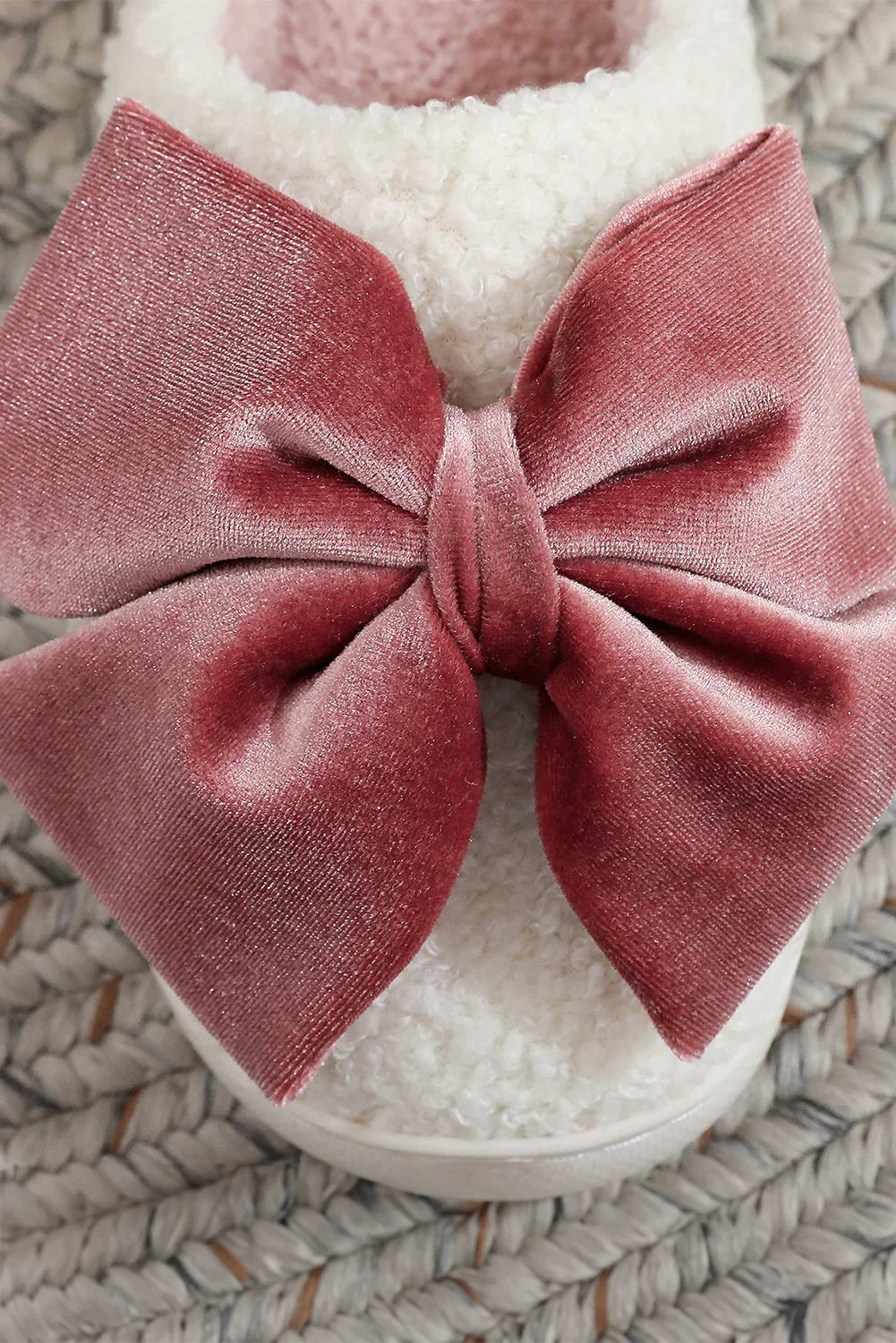 Close-up of white fluffy slipper with large dusty pink velvet bow on braided rug