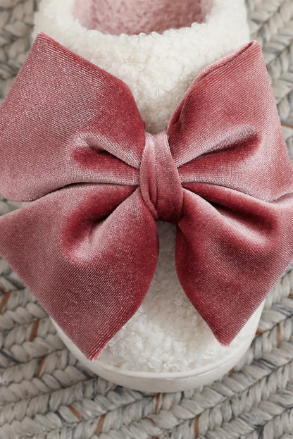 Close-up of white fluffy slipper with large dusty pink velvet bow on braided rug