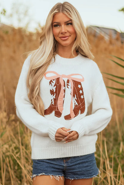 Blonde woman outdoors wearing white sweater with brown cowboy boots design and denim shorts