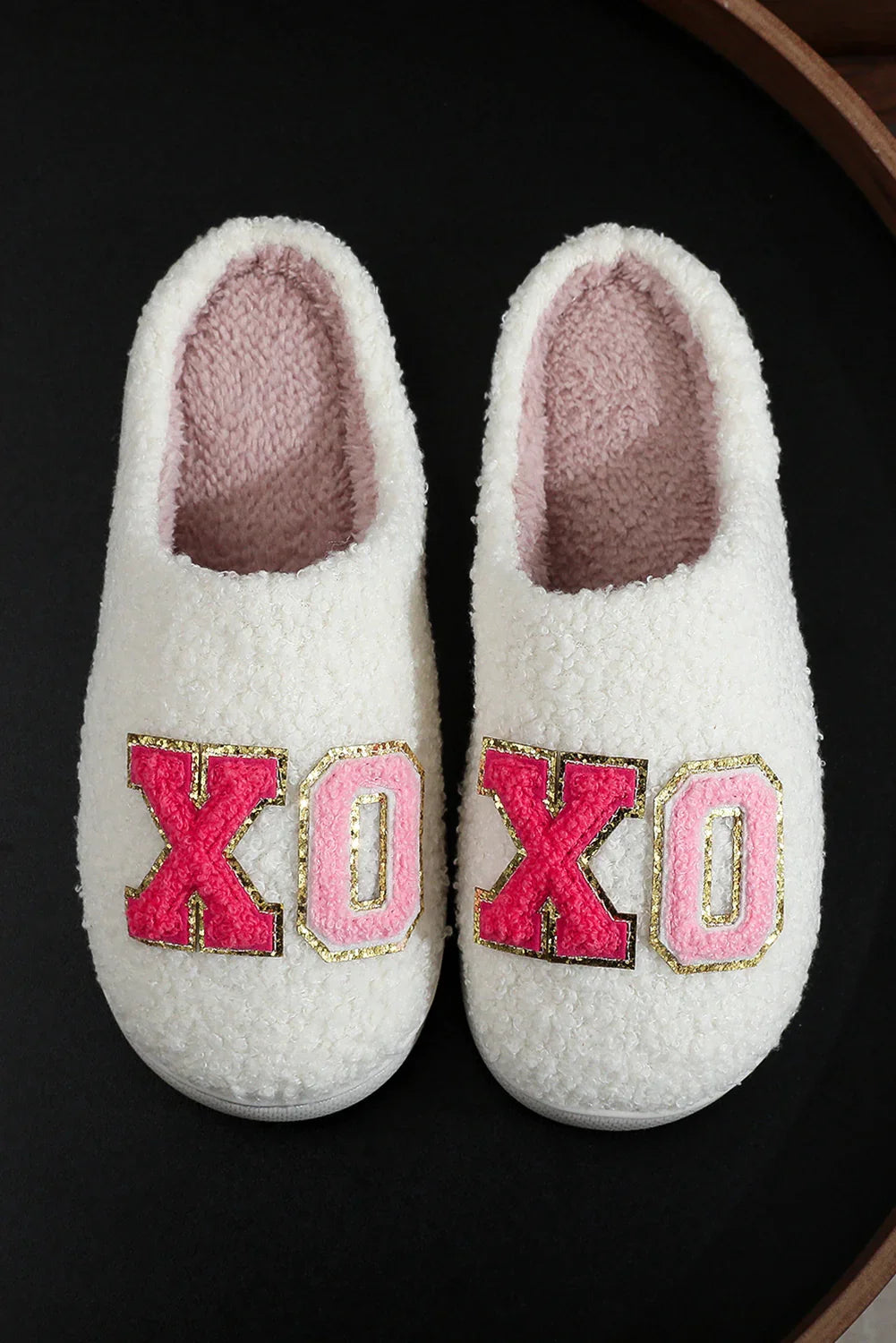 Cozy white fuzzy slippers with pink and red X and O patches on black background