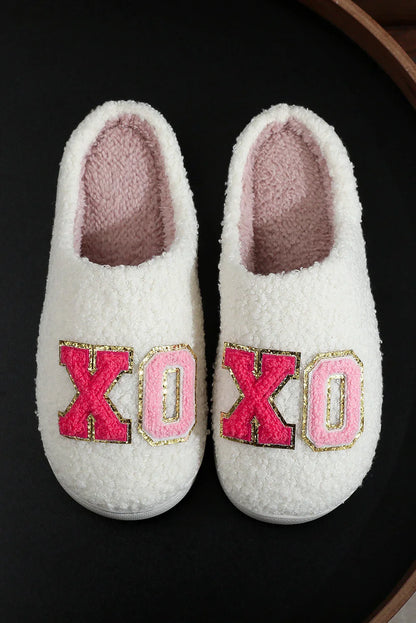 Cozy white fuzzy slippers with pink and red X and O patches on black background