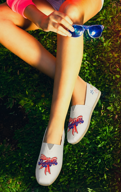 Person wearing white shoes with red, white, and blue America text and red and white strip bow designs a Bow design sitting on grass