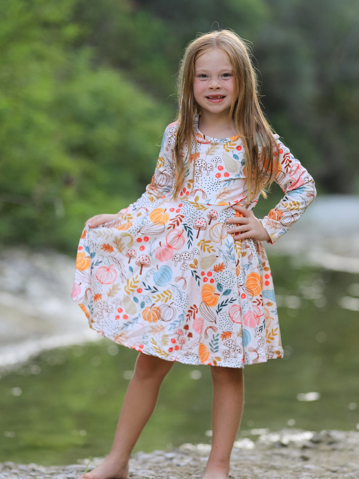 Girls Fall Dress | Pumpkin & Leaf Print: Model holding skirt beside water