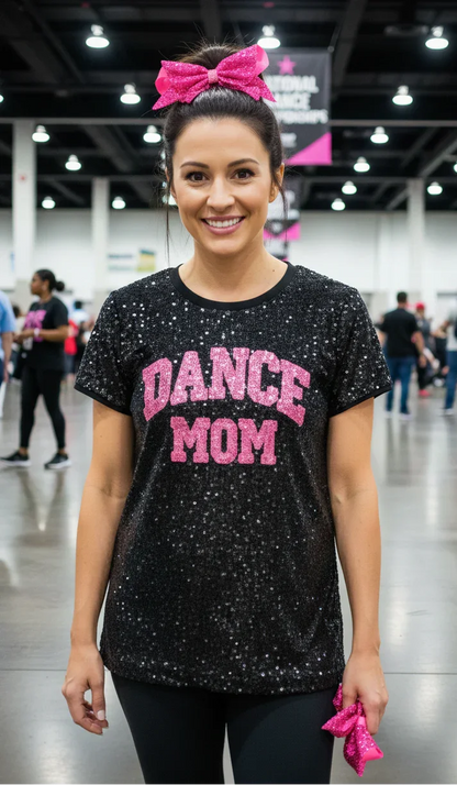 Woman wearing a black 'DANCE MOM' shirt with pink text in a convention center setting.