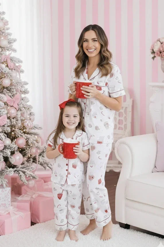 Woman and child in matching pajamas holding red mugs in a festive room with a Christmas tree and presents.