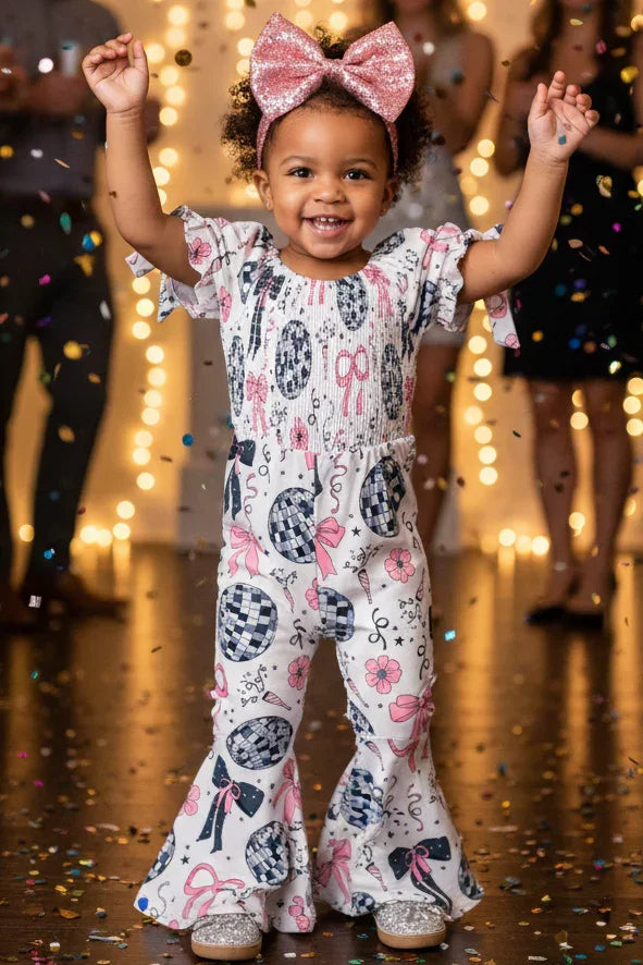 Child in a decorated room with lights and confetti, wearing a floral onesie and pink bow.