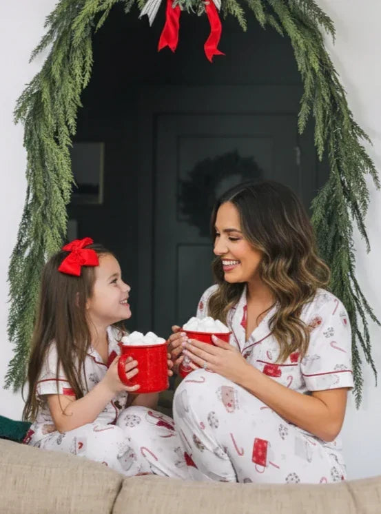 Woman and child in matching pajamas holding hot cocoa in front of a decorated Christmas door.