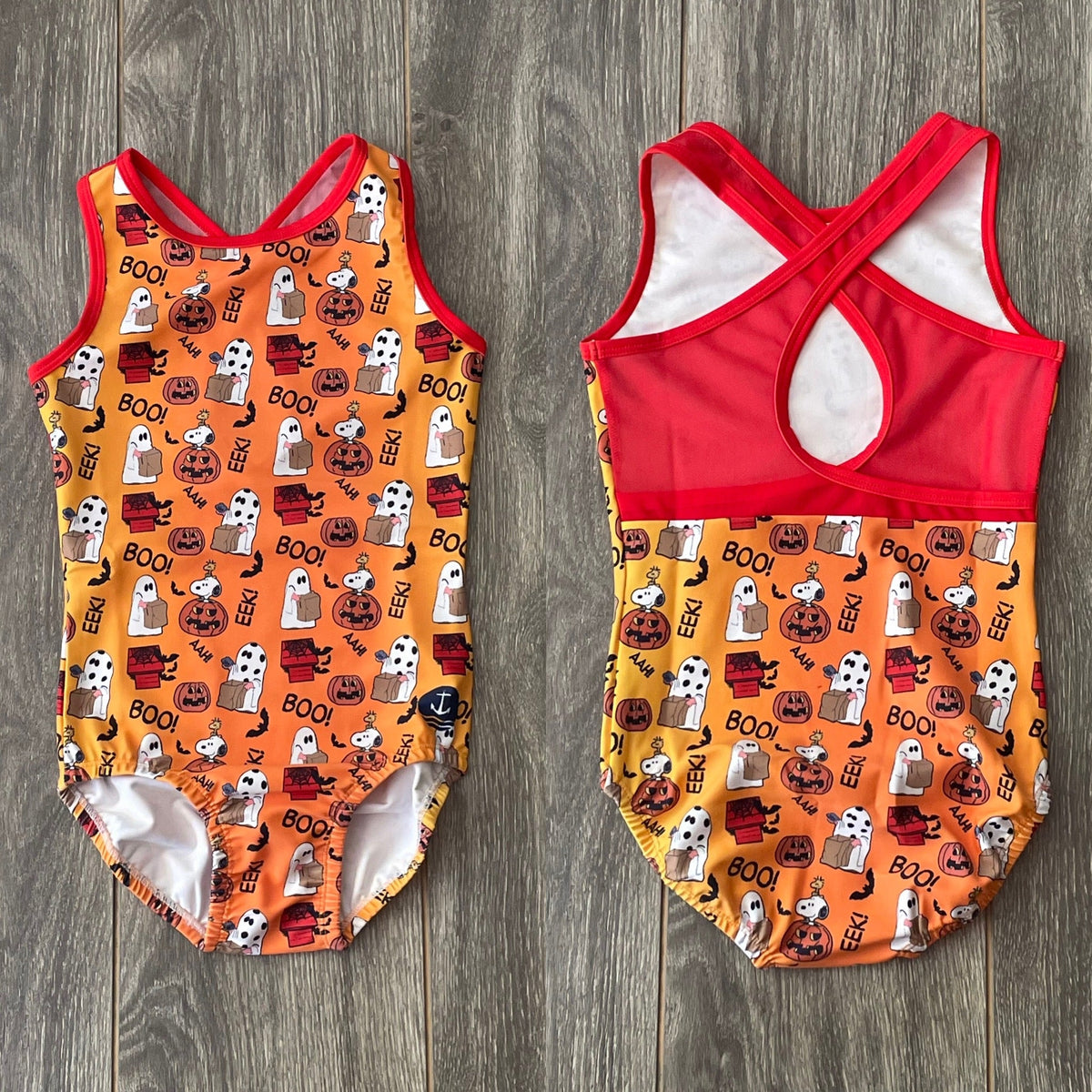 The Great Pumpkin Snoopy Halloween leotard front and red crossover mesh-back views on a wood background